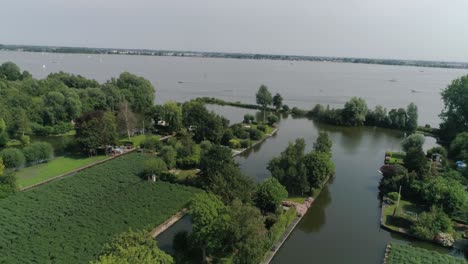Aerial-Slomo-shot-of-Green-Dutch-Countryside-with-Small-Boats,-Streams-and-Lake,-during-Sunny-Weather-and-Small-Town-in-background