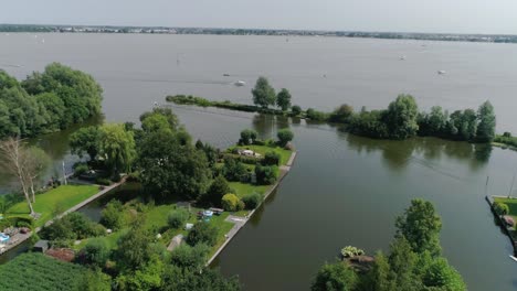Aerial-Slomo-shot-of-Green-Dutch-Countryside-with-Small-Boats-and-Lake,-during-Sunny-Weather-and-Small-Town-in-background