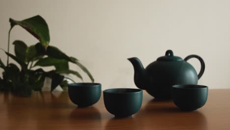 Minimaler-Hintergrund-Eines-Grünen-Japanischen-Teesets-Mit-Dampf-Aus-Den-Tassen,-Auf-Einem-Holztisch,-Mit-Einer-Pflanze-Im-Rücken