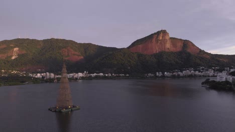Panning-movement-up-showing-the-Rio-de-Janeiro-city-lake-with-in-the-middle-the-tallest-floating-Christmas-tree-of-2018-with-in-the-background-the-Corcovado-mountain-with-the-Christ-statue-at-sunrise