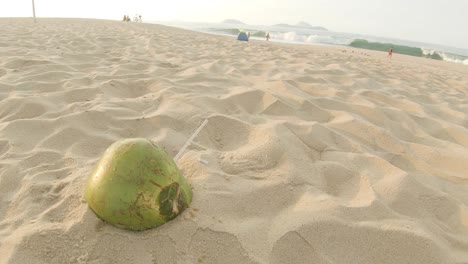 Rotating-around-solitary-empty-coconut-with-a-transparent-plastic-straw-sticking-out-left-behind-on-the-beach