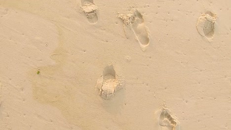 Birds-eye-top-down-view-following-various-imprinted-bare-footsteps-and-shoe-soles-on-a-pristine-beach
