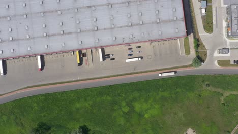 Aerial-Shot-of-Truck-with-Attached-Semi-Trailer-Leaving-Industrial-Warehouse--Storage-Building--Loading-Area-where-Many-Trucks-Are-Loading--Unloading-Merchandise