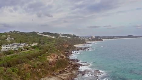 Aerial-drone-slow-descending-shot-of-rugged-coast-at-Coolum-with-cloudy-sky
