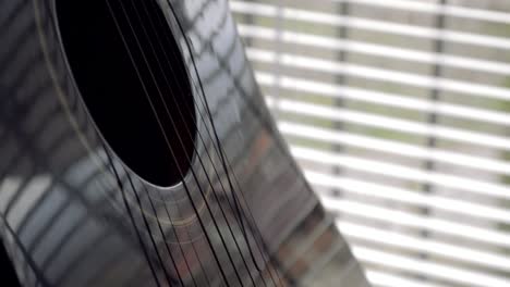 Black-shiny-acoustic-guitar-on-a-stand-by-the-window,-CLOSE-UP