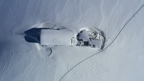 Aerial-view-looking-down-onto-a-snow-covered-mountain-shed---barn-while-slowly-rising-up