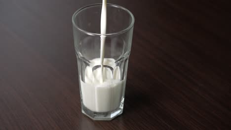 Pouring-cow-milk-into-a-tall-glass-on-a-wooden-table