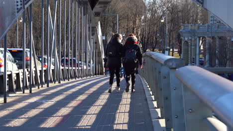 Couple-of-Girls-Walks-Across-the-Mindaugas-Bridge-Dressed-in-Dark-Color-Warm-Winter-Clothes