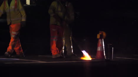 Slow-motion-view-of-a-road-worker-using-a-Thermal-lance-to-burn-white-lines-from-a-main-road-before-repainting-at-night