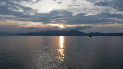 Schöne-Vietnamesische-Landschaft-Eines-Goldenen-Sonnenuntergangs,-Der-Sich-über-Dem-Ozean-Mit-Bergen-Und-Traditionellem-Fischerboot-Widerspiegelt
