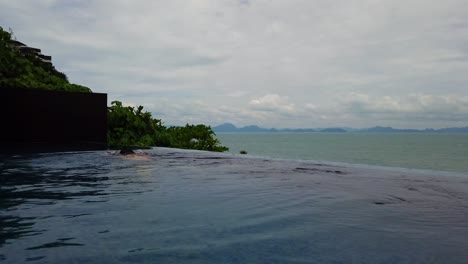 Asian-Man-swimming-at-a-Infinity-Pool-overlooking-a-Beautiful-Ocean