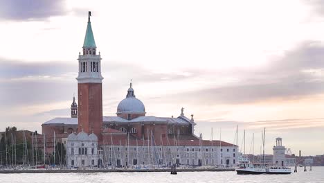 Breiter-Schuss-Von-Booten,-Die-Bei-Sonnenuntergang-An-Der-Kirche-Von-San-Giorgio-Maggiore-In-Venedig-Vorbeifahren