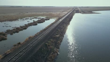 Empty-train-tracks-on-the-flat-prairie-with-sun-on-a-pond