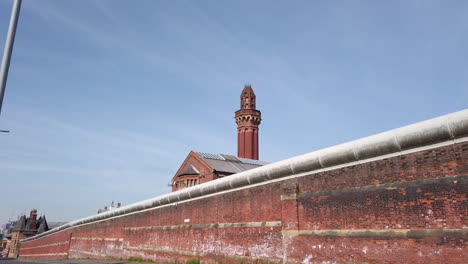 Tilt-Reveal-Shot-of-Perimeter-Security-Wall-at-HM-Prison-Manchester,-England-a-High-Security-Prison-also-known-as-Strangeways-on-Sunny-Day