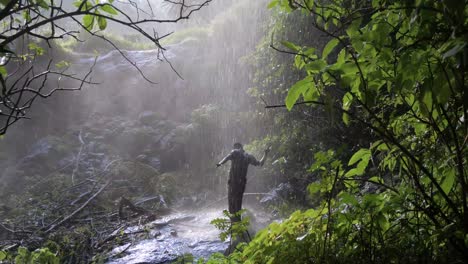 Slow-motion-wide-shot-of-a-happy-African-man-dancing-under-a-tropical-waterfall-shower