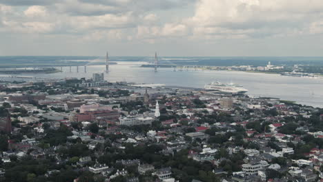 Aerial-pan-across-downtown-Charleston,-South-Carolina,-USA-with-the-Ravenel-Bridge-and-a-cruise-ship-in-the-background