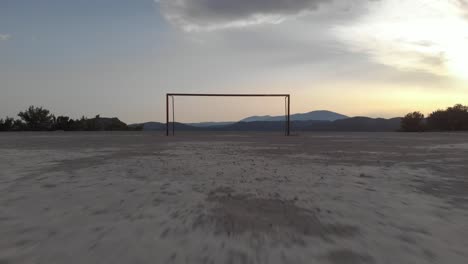 Aerial:-drone-flying-towards-empty-football-goal-close-over-hard-ground