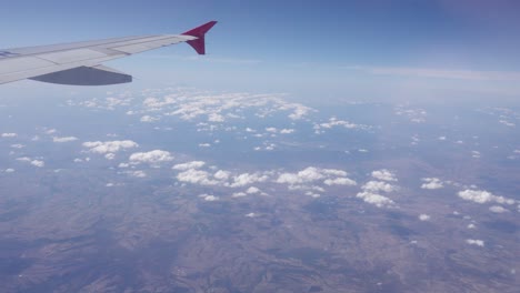 Eine-Statische-Ansicht-Eines-Flugzeugflügels,-Der-Hoch-über-Den-Wolken-Und-Dem-Boden-Fliegt