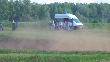 Autocross-cars-compete-in-amateur-racing-on-the-dirt-track-in-sunny-summer-day,-people-watching-cars-passing-by,-medium-shot-from-a-distance