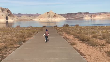 Niño-Felizmente-Saltando-De-Alegría-A-La-Playa-En-El-Lago-Powell,-Arizona