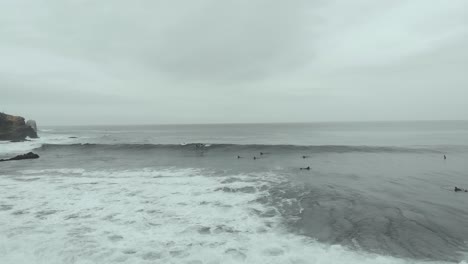 Aerial-Panorama-of-the-waves-and-surfers-on-a-cloudy-day-at-the-beach,-Pichilemu,-Chile