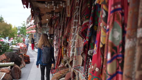 Woman-tourist-walking-past-a-popular-Turkish-rug-ship-in-Goreme,-Turkey-with-authentic-Turkish-rugs-hanging