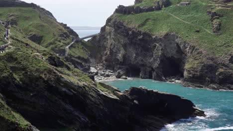 People-on-vacation-walking-on-top-of-a-cliff-along-the-path-that-leads-to-the-ruins-of-Tintagel-castle-and-bridge-to-the-island-in-Cornwall