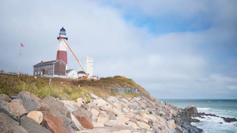 Side-view-of-the-Montauk-Point-lighthouse-and-the-rocks-on-the-beach-on-a-partly-cloudy-day