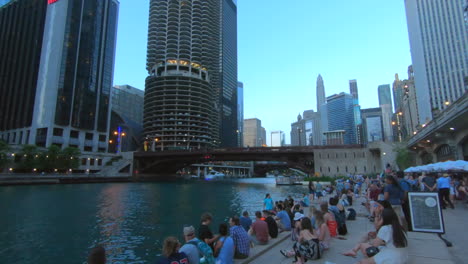 Chicago-Riverwalk-view,-Usa,-United-States,-by-the-river,-people,-tourists-sitting,-watching-river-and-boats,-summer-time,-downtown,-cityscape,-buildings-and-bridge