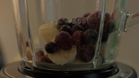 Woman-puts-a-pieces-of-berries-and-banana-in-the-bowl-of-a-blender,-close-up-shot