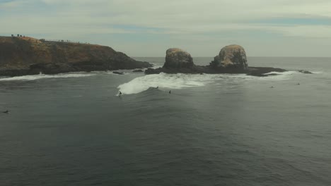 Luftaufnahme-Eines-Surfers,-Der-An-Einem-Dunklen,-Kalten-Tag-In-Pichilemu,-Chile-4k,-Neben-Riesigen-Felsen-Auf-Einer-Welle-Reitet