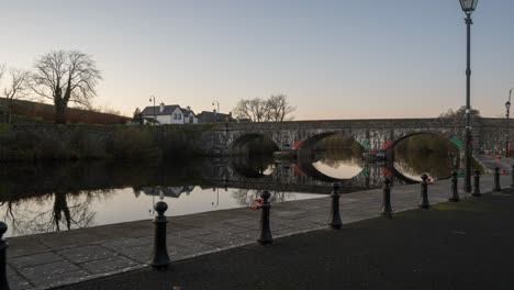 Holy-Grail-or-Day-to-Night-Time-Lapse-of-town-village-with-bridge-and-street-lights-along-a-river-in-Ireland