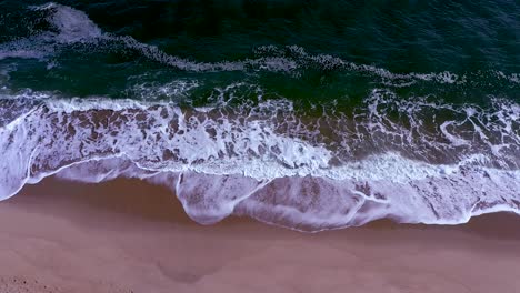 slow-upward-tilting-cinematic-aerial-shot-moves-from-beach-waves-to-reveal-the-deep-blue-ocean-and-horizon