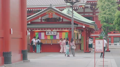 Turistas-Caminando-Con-Chicas-Japonesas-En-Kimono-Dibujando-Fortuna-Escrita-En-O-mikuji-Encontrada-En-El-Santuario-Senso-ji-En-Asakusa,-Tokio,-Japón