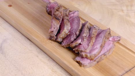 Slow-Motion-Slider-Shot-of-Placing-Sliced-Medium-Rare-Steak-on-a-Wooden-Serving-Platter