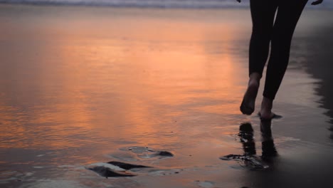 Barefoot-woman-in-leggings-walks-towards-ocean-on-sunset-evening,-Azores-beach