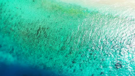 Blue-turquoise-sea-texture-with-calm-clear-water-over-coral-reefs,-reflecting-sunlight-of-a-hot-summer-day-in-Caribbean