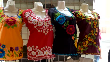 Camera-turns-to-left-as-it-moves-right-showing-huipil-Mexican-blouses-for-women-in-a-shop-in-Merida,-Mexico