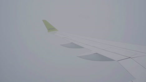 Air-Baltic-flying-in-bad-foggy-weather,-airplane-wing-shot-from-inside-the-aircraft,-intense-fog