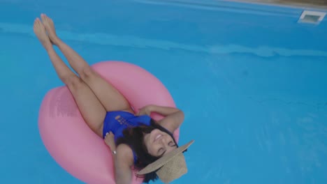 Cheerful-attractive-girl-enjoys-vacations-on-inflatable-pink-ring-on-swimming-pool