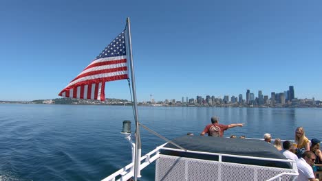 Back-of-yacht-with-American-flag-and-city-Seattle-in-background,-slow-motion