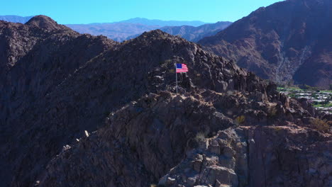 Una-Bandera-Estadounidense-Ondeando-Al-Viento-En-La-Cima-De-Una-Gran-Montaña