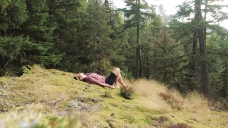 A-beautiful-young-adult-woman-lies-down-on-green-and-mossy-forest-ground-while-enjoying-sunshine-and-calmness