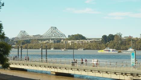 people-crossing-and-riding-bike-on-City-Botanic-Gardens-Riverwalk-and-River-in-Brisbane-CBD,-brisbane-botanic-garden-new-bikeway