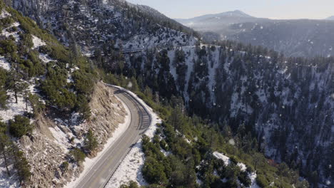 Aerial-Shot-of-Winding-Mountain-Road-in-Snowing-Winter-Landscape