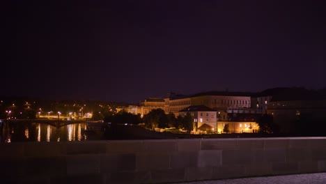 Nighttime-on-a-bridge-in-Prague,-popular-tourist-destination,-two-girls-looking-down-at-water,-pan-left