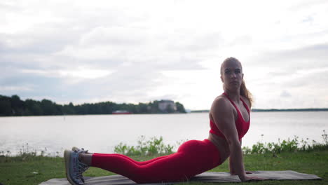 Young-woman-in-red-sportswear-sitting-on-yoga-mat-outside-doing-exercises-and-practicing-yoga