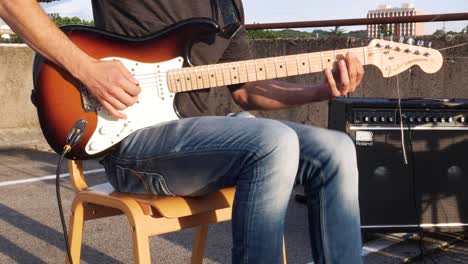 Nahaufnahme-Eines-Gitarristen,-Der-E-Gitarre-Auf-Der-Parkgarage-Spielt,-Mit-Sichtbaren-Wohnblöcken-Und-Einigen-Baumwipfeln-Im-Hintergrund