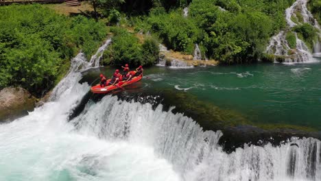 River-rafting-teams-go-down-a-jump-at-Strbacki-Buk-waterfall-in-the-Una-river-at-the-border-with-Bosnia---Herzegovina,-Aerial-pan-left-shot
