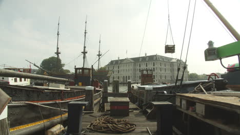 Detalles-De-Un-Embarcadero-De-Madera-En-Amsterdam,-Países-Bajos-Con-Vistas-Al-Museo-Marítimo-Nacional-Y-La-Réplica-Del-Barco-De-Amsterdam-En-El-Fondo---Tiro-Inclinado-Hacia-Abajo